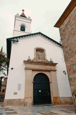 Iglesia de La Veracruz su fachada principal con puerta de marco en círculo, de color verde y que está cerrada. En la vista de abajo hacia arriba se nota un cielo blanco.  
