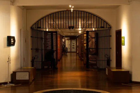 National Museum of Colombia, interior corridor with wooden display cases on both sides, a wooden floor, and separated by a half-open iron gate.