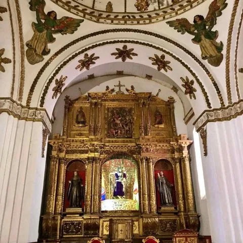 Church of St. Augustine, interior view of the colonial atrium and the altarpiece decorated with angels and floral designs on the oval-shaped ceilings. In the background, wooden religious figures can be seen.