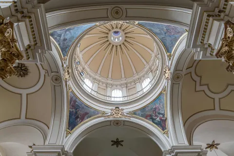 Catedral Primada de Colombia, cúpula del atrio vista desde abajo en la que destaca la fina mampostería y los murales entre azules y rojos con figuras de personas. La cúpula destaca el decorado en forma de estrella y 3 ventanales con luz blanca.
