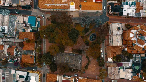 Usaquén Square, aerial wide shot taken by drone showing the rooftops of the houses, the small soccer field, lush trees, and streets. No people are visible.