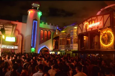 Theatron de noche intrior plazoleta llena de personas alrededor de fachadas iluminadas.