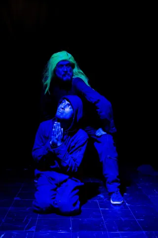  Barraca Teatro con actores en escena arrodillados miran de frente. Uno tiena una peluca amarilla.