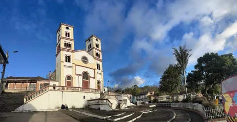  Iglesia Parroquial Nuestra Señora del Rosario - Junin vista desde abajo en la plazoleta rodeada de árboles con dos personas sentadas afuera y un cielo de atardecerazul  con algunas nubes.