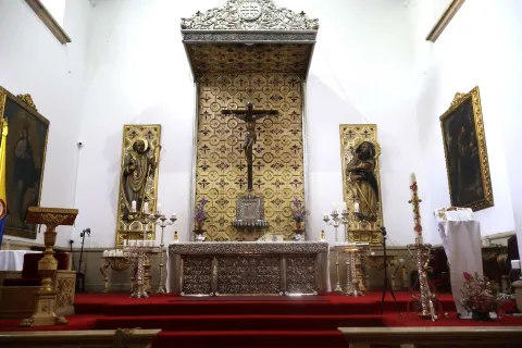 Iglesia de La Veracruz en su interior blanco con el altar con un Cristo en el centro y dos figuras religiosas a los lados. El psio está cubierto con un tapeqte roj.