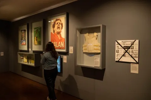 National Museum of Colombia, interior hall exhibiting images of political leaders who were victims of violence, such as Luis Carlos Galán, Carlos Pizarro, and Bernardo Jaramillo. A display case holds a bulletproof vest, while a woman is seen from behind observing the works.