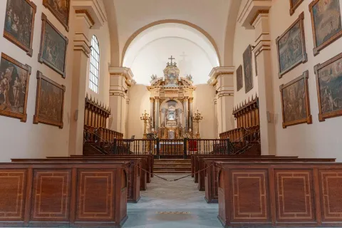 Catedral Primada de Colombia, capilla interior con dos paredes repletas de cuadros, dos filas de sillas en madera y al fondo un altar dividido por una reja metálica. El salón está vacío.