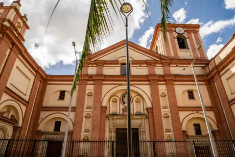 St. Ignatius Church, close-up front view of the façade. In front, there are three electric poles, two palm branches, and a blue sky.