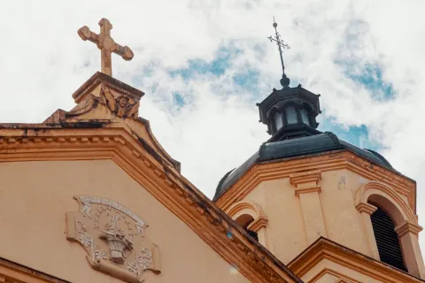  Iglesia de la Candelaria Iglesia de la Candelaria colonial con la parte alta de su fachada en primer plano, se resalta la punta del frente coronada por una cruz y una torre con su cúpula negra y una cruz metálica encima. 