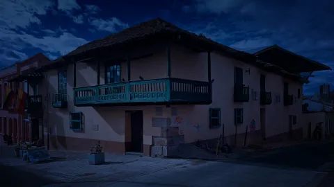 Casa esquinera colonial fachada rosa con balcones verdes, dos palomes sobre el principal y un tono azul como de anochecer. 
