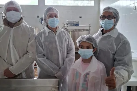 un hombre, dos mujeres y un niño con cofias y tapabocas en una cocina industrial.