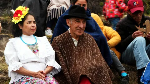 En el campo, un hombre, adulto mayor, y una mjujer campesina sentados sobre una montaña.