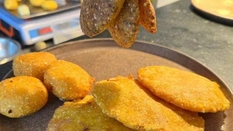 Tres arepas de huevo en primer plano sobre un plato café, acompañadas de otrAs tres arepas y tres pasteles.
