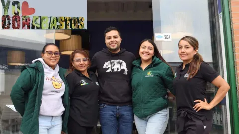 Grupo de cuatro mujeres y un hombre que abrazados sonríen. Hay un logo que dice yo amo Corabastos