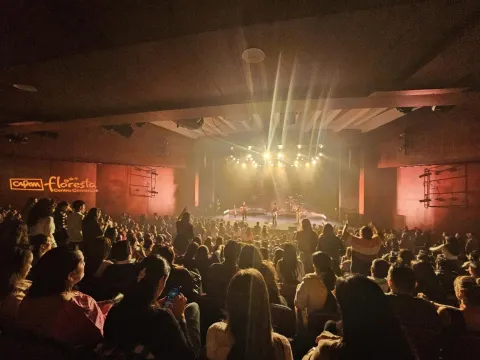 Teatro Cafam interior escenario lleno, semi oscuro con luces reflectivas y un grupo musical en el escenario.  