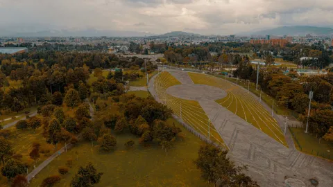 Simón Bolívar Park, a wide aerial view from a drone, showing the events plaza surrounded by leafy trees, with city buildings and a few mountains in the background.