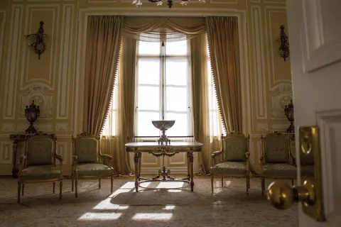 Salón pintado de amarillo con estilo clásico en el que sobresalen 4 sillas y una mesa con un jarrón. Al fondo hay un gran ventanal desde donde ingresa luz natural. 