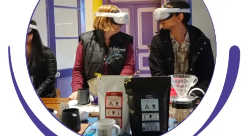 Dos personas con cámaras de 3D al frente unos frascos, pocillo y bolsas con cacao. 