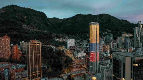 At dusk, the Colpatria Tower is illuminated with the colors of the Colombian flag, with a view from west to east showing several tall buildings and the eastern hills in the background.