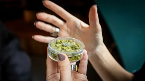 Dos manos de mujer en primer plano sostiene un recipiento con un ingrediente verde en polvo.
