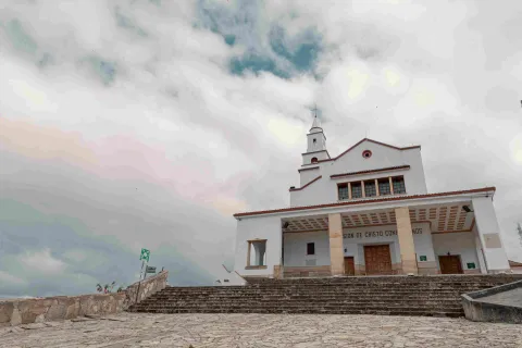 Fachada blanca de la iglesia de Monserrate vista de frente, puertas cerradas y el cielo blanco.