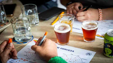 Sobre una mesa hay un papel en el que están rayando un hombre y una mujer. Parece ser el registro de la cata de cerveza, pues hay varios vasos con cerveza y otros con agua.