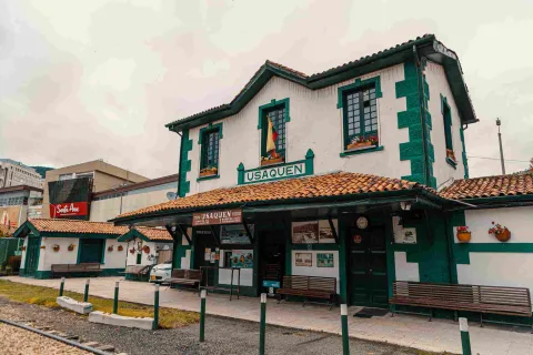 Estación de tren en Usaquén, con una casa que es la taquilla, con fachada blanca con rayas verdes, techo en teja de barro y dos avisos que dicen: "Usaquén".