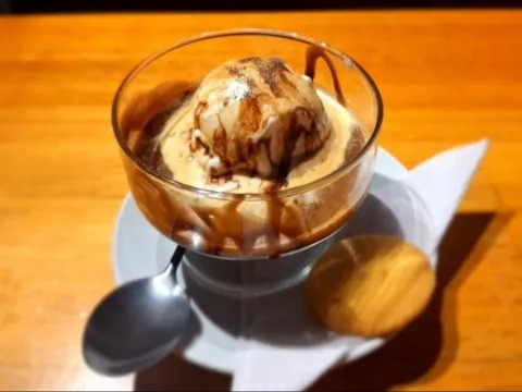 Una copa de helado con café, una galleta dorada y una cucharita, sobre un plato redondo.
