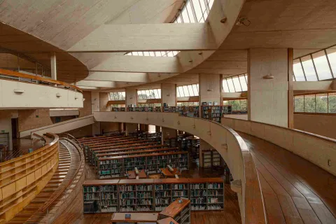 Library interior featuring circular wooden walkways, windows along the sides, and a room below with bookshelves full of books.