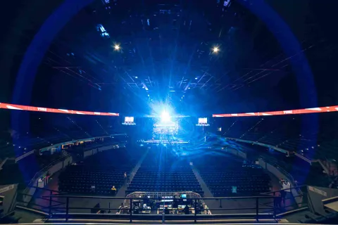 Escenario interno en el que se ven tribunas desocupadas y un haz de luz brillante azul que viene desde la tarima.