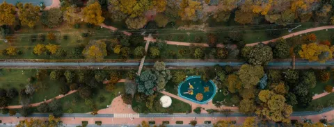 Parque visto desde arriba con un largo caño de agua en el centro y un parque infantil rodeado por árboles frondosos.