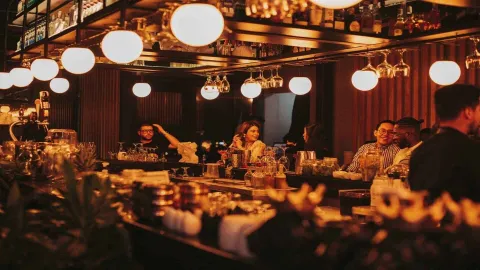  Un bar animado y concurrido, iluminado cálidamente, donde la gente disfruta de bebidas y conversaciones.