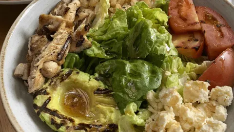 Ensalada fresca con pollo a la parrilla, aguacate, tomate, lechuga y queso feta, aderezada con vinagreta.