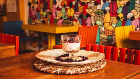 Un postre de capas con salsa de frutos rojos, servido en un plato decorado sobre una mesa de madera.
