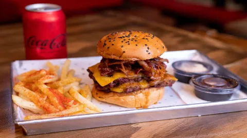 Una jugosa hamburguesa doble con queso y cebolla caramelizada, acompañada de papas fritas y una Coca-Cola.