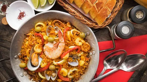 Una vibrante paella de mariscos con arroz, mejillones, calamares y gambas, servida con pan y lima.
