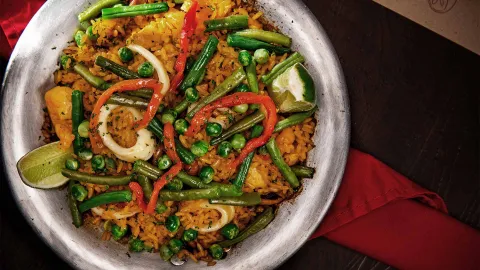 Una paella vegetariana colorida con arroz, judías verdes, guisantes, pimientos y calamares falsos.
