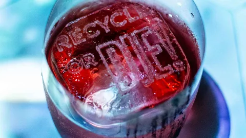 Un cubito de hielo grabado con el mensaje "RECYCLE OR DIE" en una bebida roja vibrante.