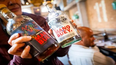 Un hombre muestra en primer plano dos botellas de licor, en las que las etiquedas dicen que es viche.