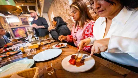 Tres mujeres jóvenes sentadas alrededor de una mesa degustando un postre. En la mesa hay copas de cristal con licor.