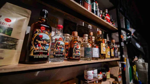 Varias botellas llenas, parece de licor, y ubicadas sobre un estante de metal y de madera.