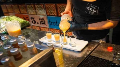 Primer plano de un mesero sirviendo chicha en cuatro copitas de cristal.