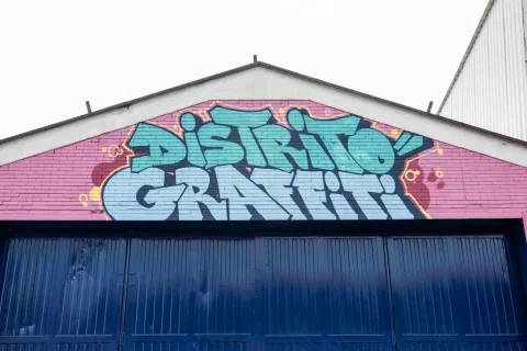 Pared de ladrillo de color rosa encima de una puerta metálica, pintada en color azul con la frase: "Distrito Graffiti".