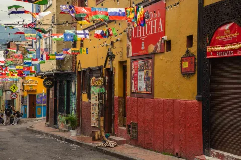 Calle con varias casas antiguas, cuyas fachadas llevan vistosos colores.Destaca un aviso con una leyenda que dice: "Chicha".