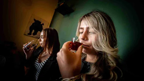  Dos Mujeres jóvenes huelen cada una, el contenido líquido de una copa de cristal.
