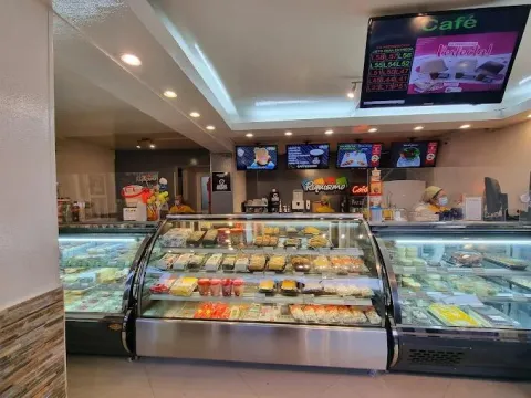 Interior de local comercial donde hay varias vitrinas con jugos y postres. Se observan 5 pantallas de televisión reproduciendo información comercial.