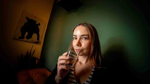 Mujer joven sonríe mientras huele el contenido líquido de una copa de cristal.