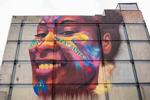  Pared de ladrillo de color blanco con el rostro sonriente de una mujer joven afro. En el rostro hay dos palabras: "Senti y Pensantes".