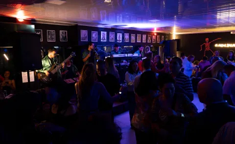 Grupo de adultos en un salón están bailando al lado de una banda musical.