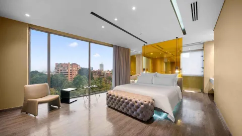 Una lujosa habitación de hotel con una cama king-size, grandes ventanales con vistas a la ciudad y un diseño contemporáneo con detalles dorados.